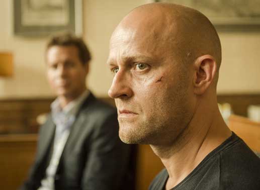 Nahaufnahme von Blochin (Jürgen Vogel), im Hintergrund Dominik (Thomas Heinze), er schaut auf Blochin. Blochin hat eine Narbe an der Wange. Bild: Sender / Stephan Rabold