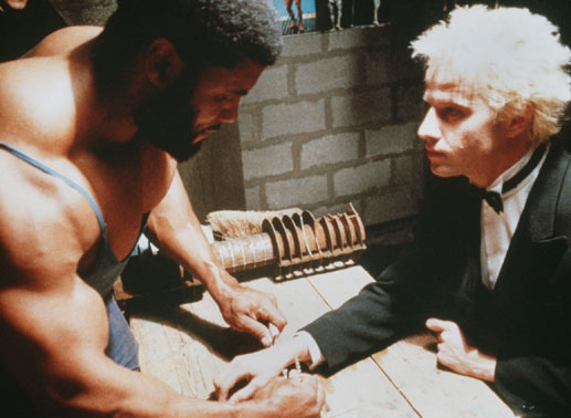 Der Bodybuilder Big Bill (Christian Gomba, li.) entfernt Freds (Christopher Lambert) Handschellen mit bloßen Händen. Bild: Sender